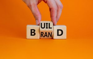 Wooden blocks spelling brand on an orange background, representing brand journalism and content marketing strategy.