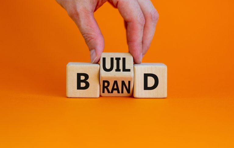 Wooden blocks spelling brand on an orange background, representing brand journalism and content marketing strategy.